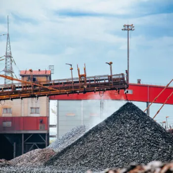 Iron briquette in factory. Excavator digs and loads hot briquetted iron into heap