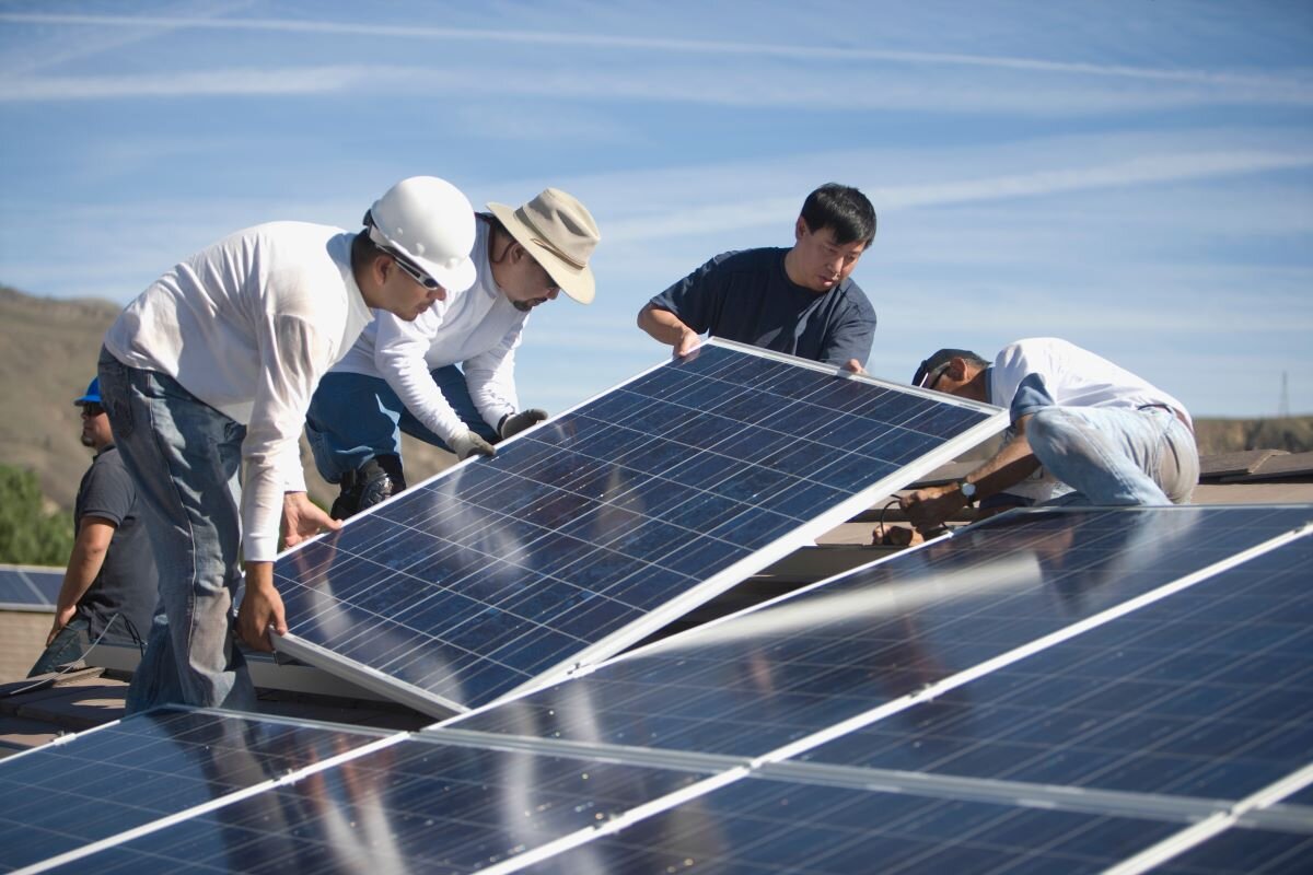 A group of engineers place the final section of a solar panel during installation in the US. Photo via Adobe.