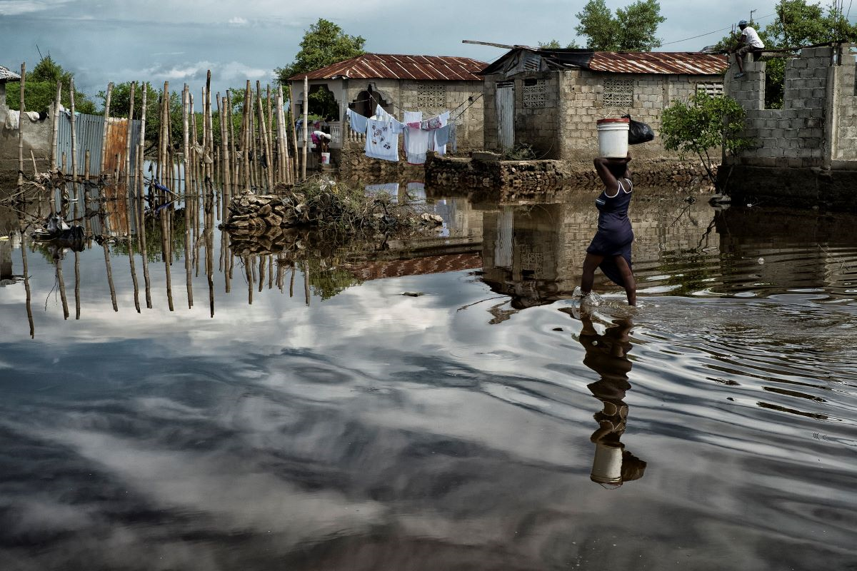 A woman carries supplies through a flooded street in Cap Haitien, Haiti, after extreme flooding. Loss and damage from climate change is hitting communities across the world.