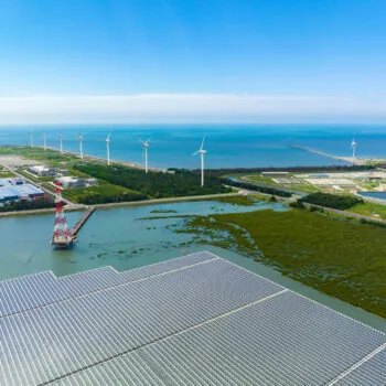 An aerial view shows a solar power plant floating on calm water, with rows of solar panels spread across the surface, capturing sunlight for clean energy.