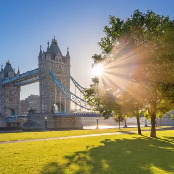 London, UK – Iconic Tower Bridge at sunrise in the morning with sunlight, tree, blue sky and green grass