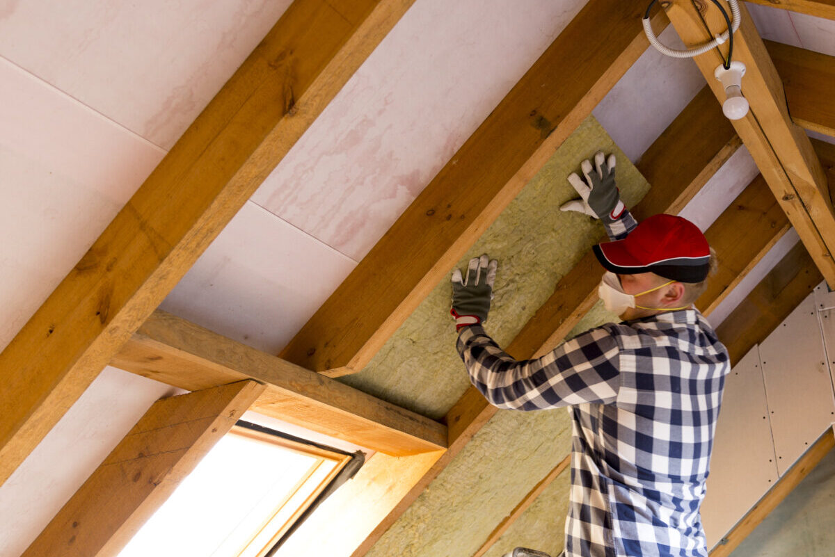 Man installing thermal roof insulation layer  – using mineral wool panels.