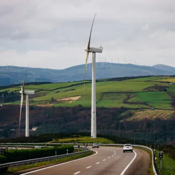 Wind turbines stand tall on rolling green hills beside a winding road, showcasing renewable energy and sustainable technology in a serene landscape