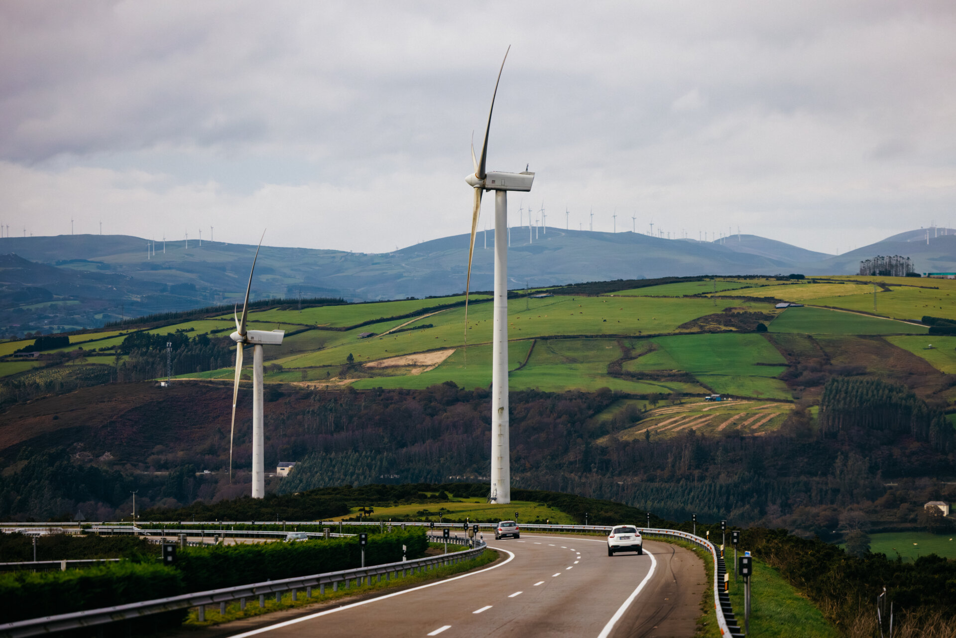 Wind turbines stand tall on rolling green hills beside a winding road, showcasing renewable energy and sustainable technology in a serene landscape