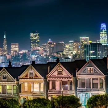 Backed by the night skyline of the city of San Francisco, California, the Victorian era houses near Alamo Square Park, are painted in colors to accentuate their architectural details.
