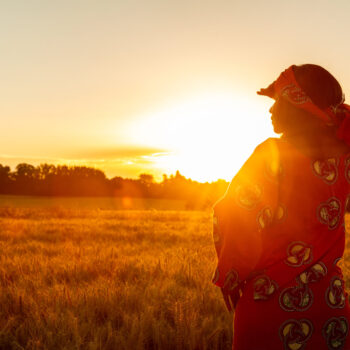 frican woman in traditional clothes standing in a field of crops at sunset or sunrise