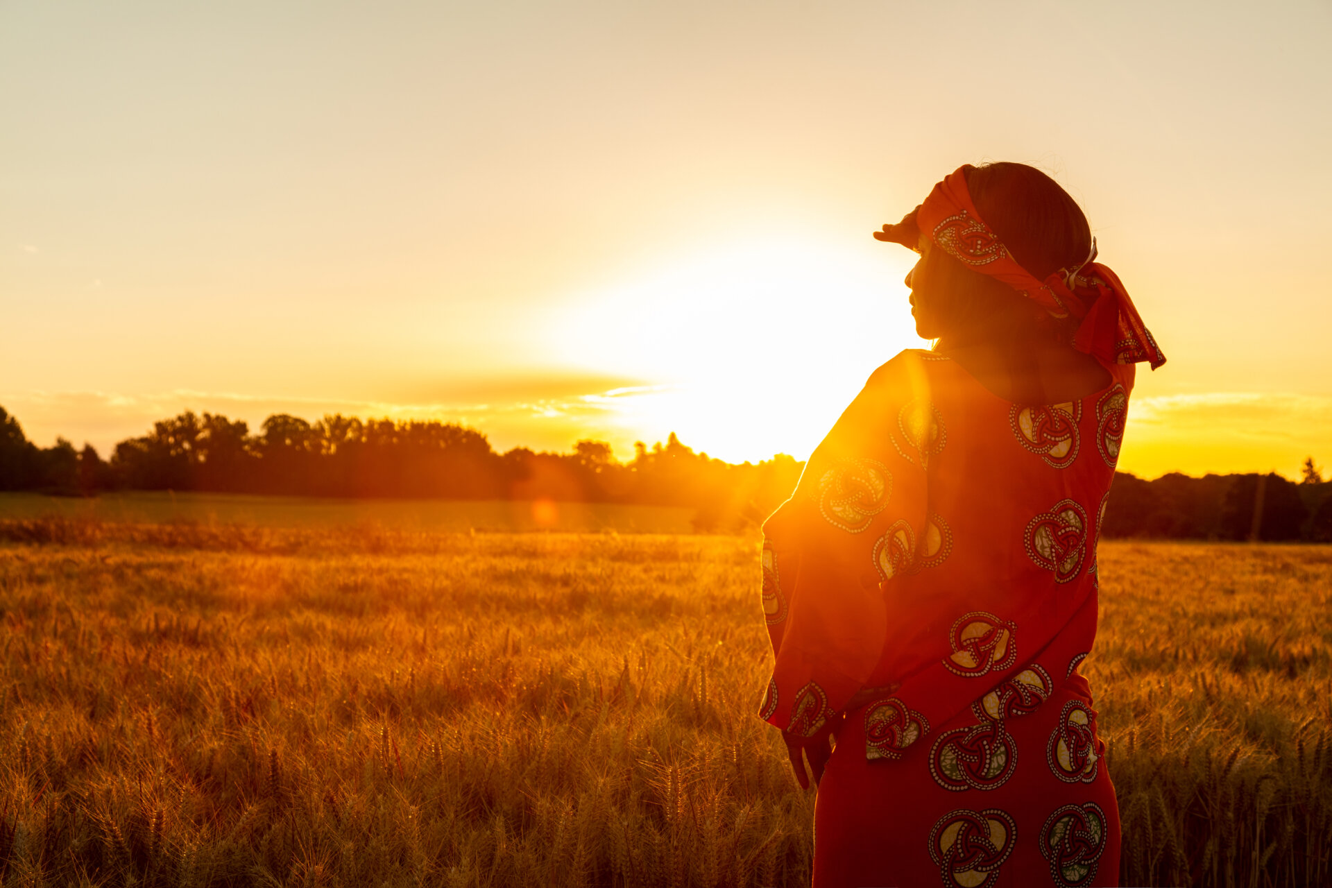 frican woman in traditional clothes standing in a field of crops at sunset or sunrise
