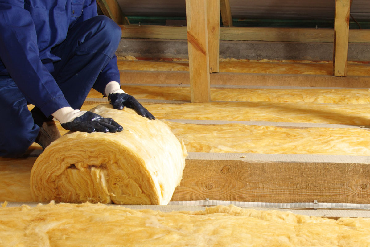 Worker thermally insulating house attic with glass wool