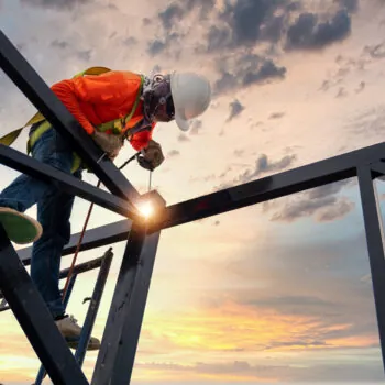 A welder is welding steel on a steel roof truss. Working at heig