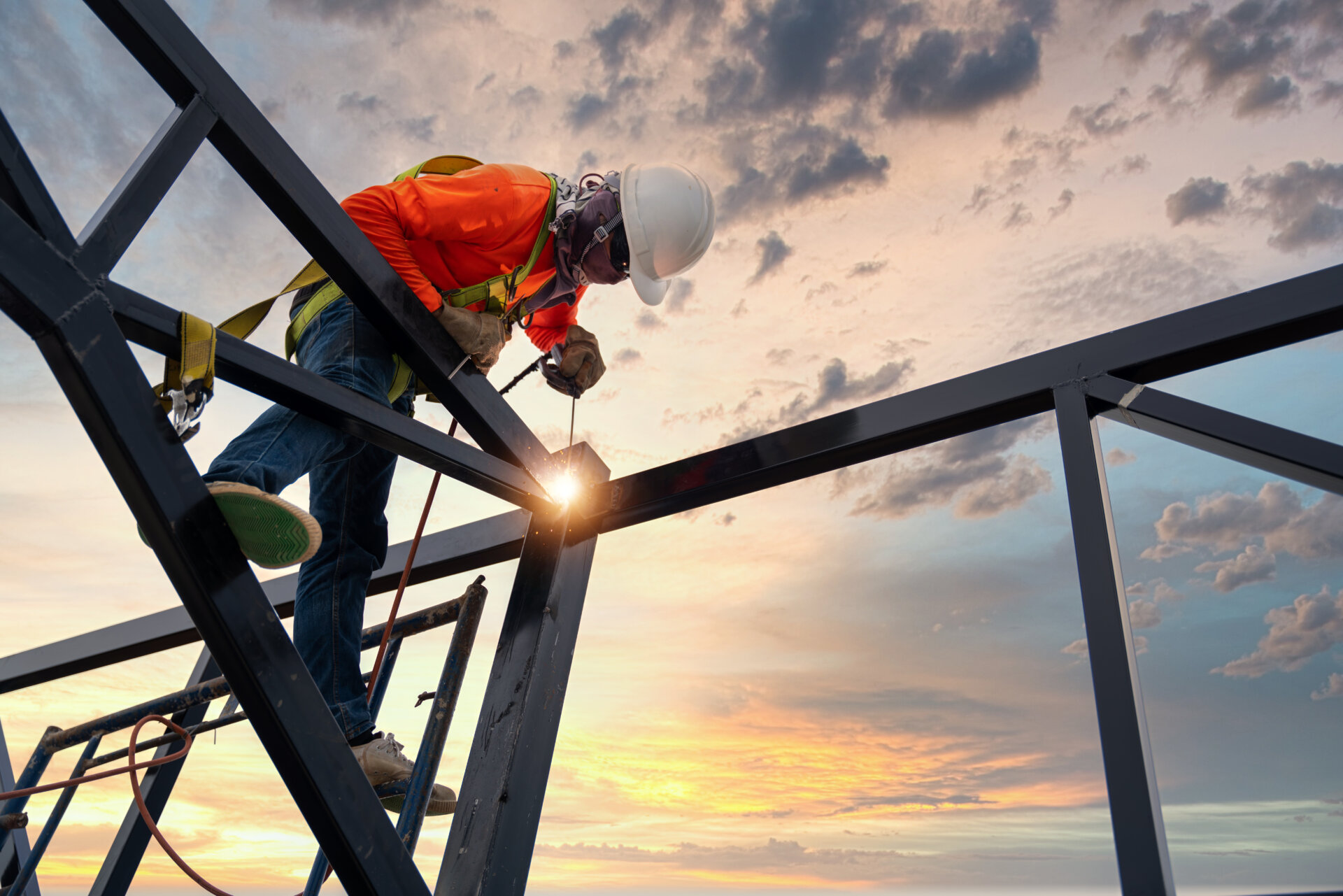 A welder is welding steel on a steel roof truss. Working at heig