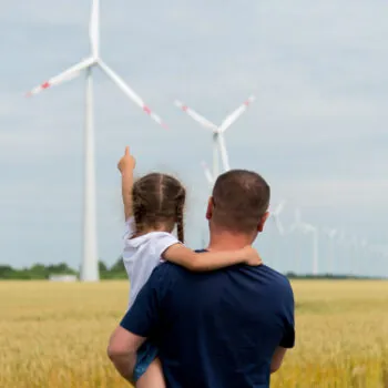 A girl and her dad look at the wind generator in the field. Ecology. Future.