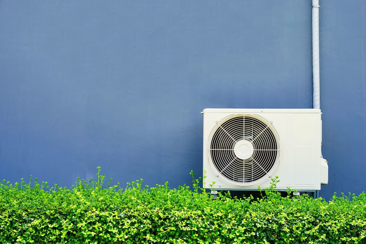 Air conditioner unit against a blue wall with green plants