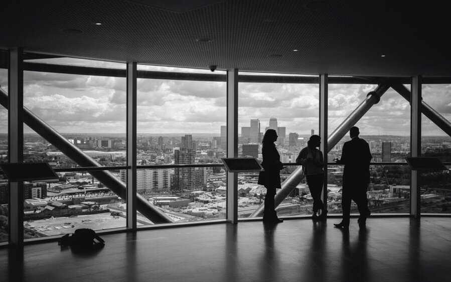 Silhouettes of people in a corporation's office. In the background there are big windows with a view to a city.