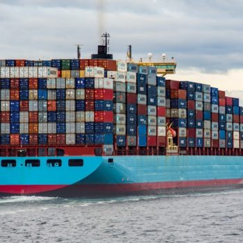 A huge blue and red cargo ship holds thousands of containers in the middle of the sea, representing global trade and its climate impacts, something that COP26 started to adress.