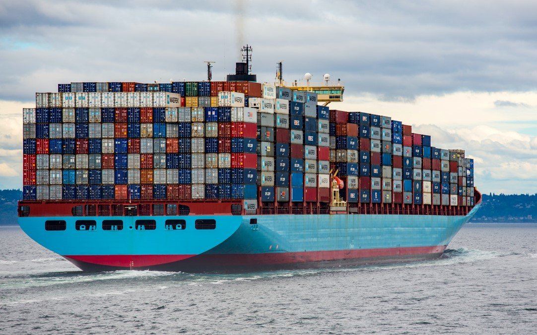 A huge blue and red cargo ship holds thousands of containers in the middle of the sea, representing global trade and its climate impacts, something that COP26 started to adress.