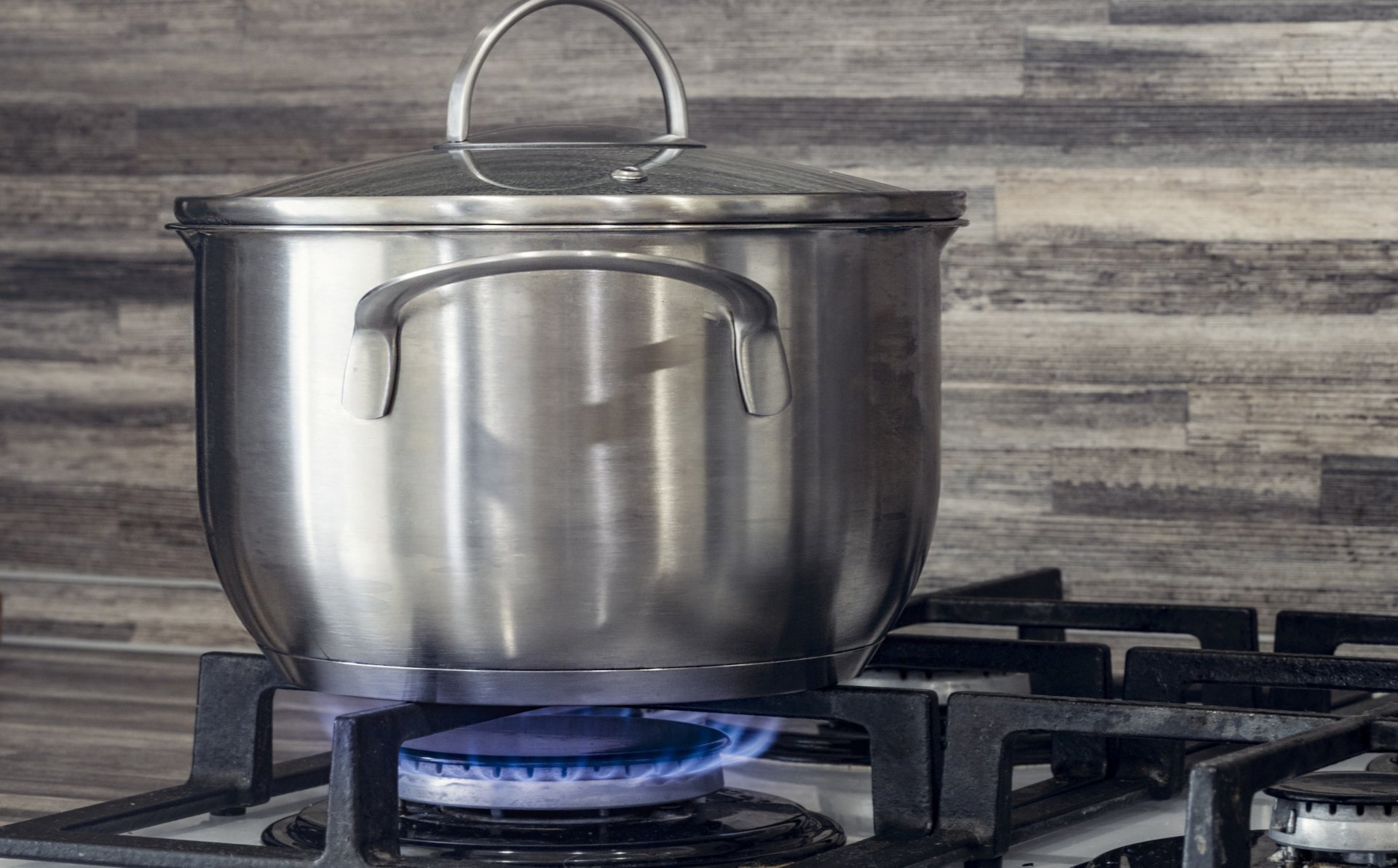 The image shows a silver cooking pot on a gas kitchen