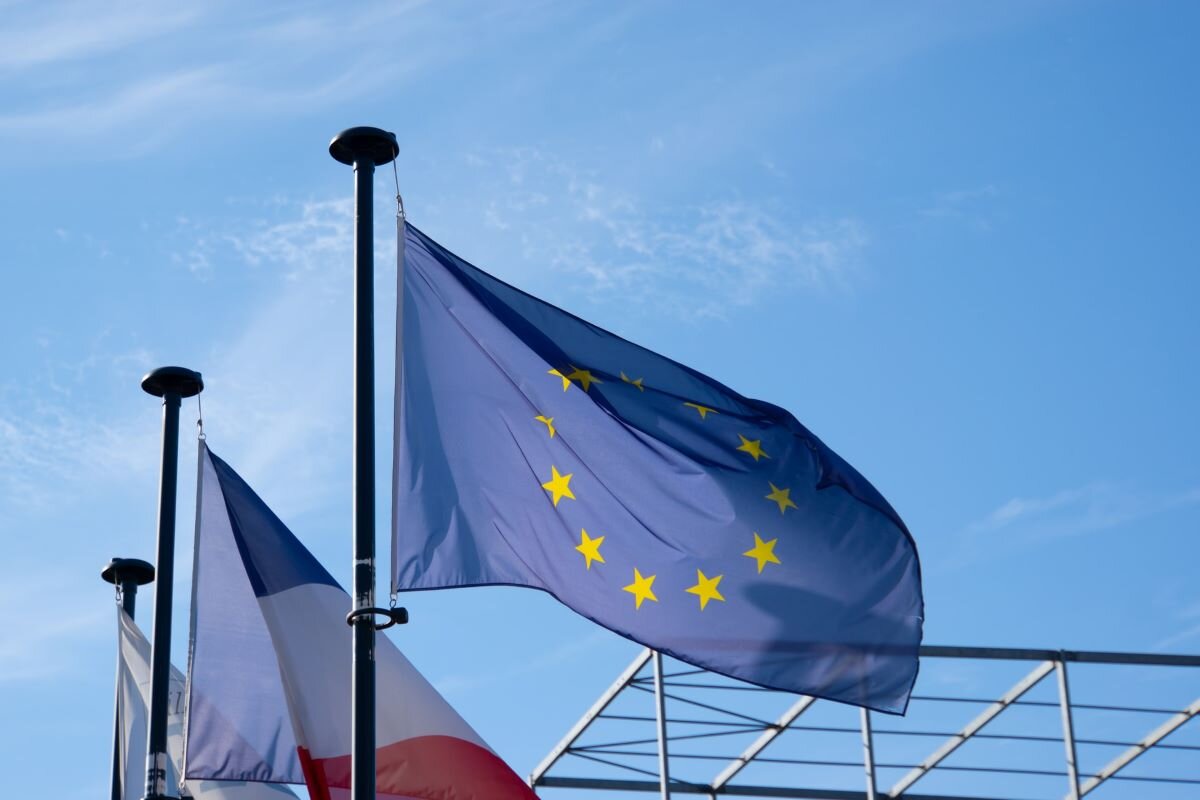 EU flag against a blue sky with the French flag and other flags behind.