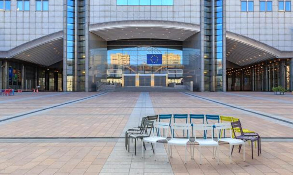 Chairls of different colours set in circle in front of the main entrance of the European Parliament in Brussels.