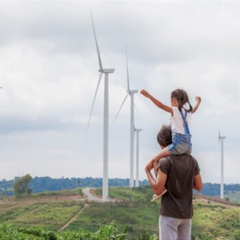 Father and daughter look at a wind turbine farm. Photo via Adobe.