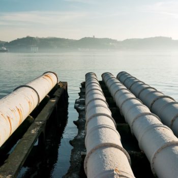 Four sun-bleached gas pipes stretch out into the distance on a lake in Lisbon, against a blue sky.