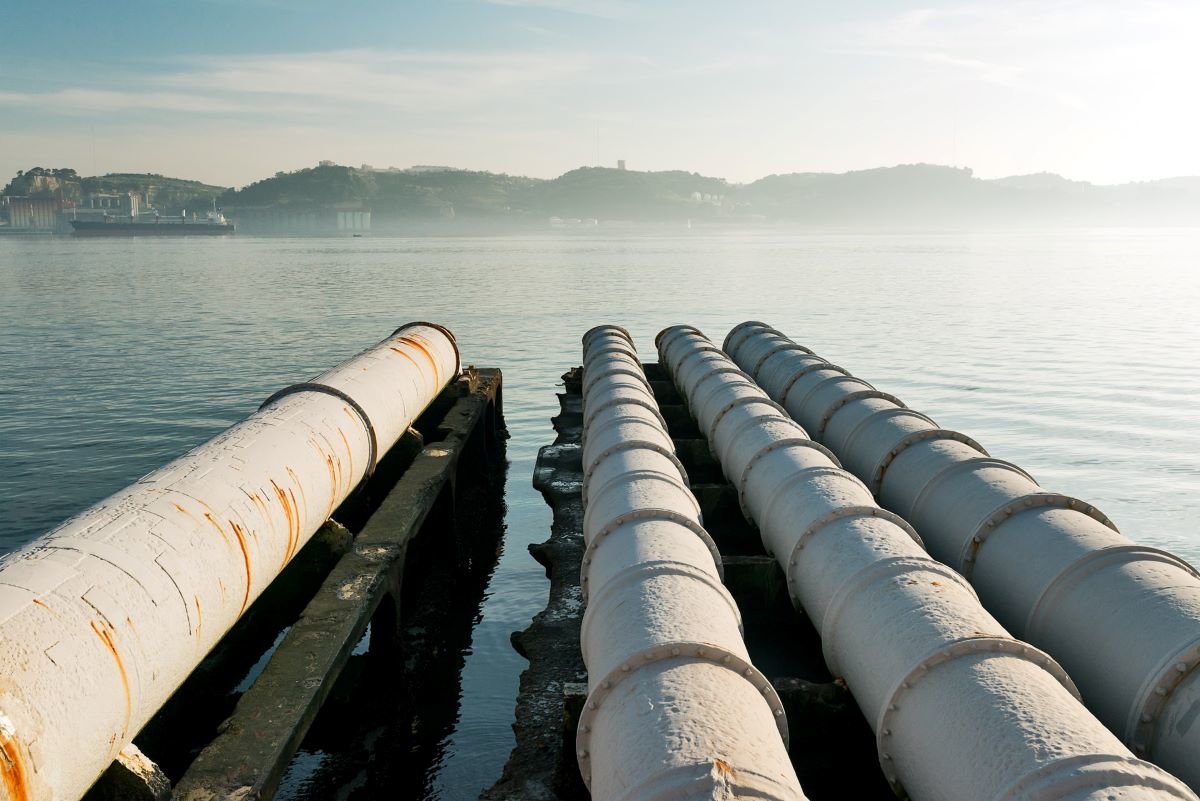 Four sun-bleached gas pipes stretch out into the distance on a lake in Lisbon, against a blue sky.