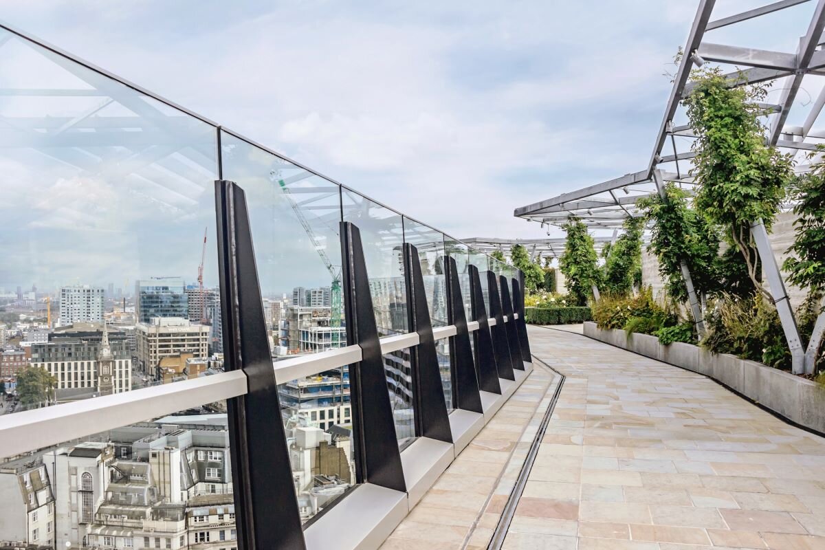 A green walkway above central London, with glass structural support with banking sctor and government buildings visible through it.