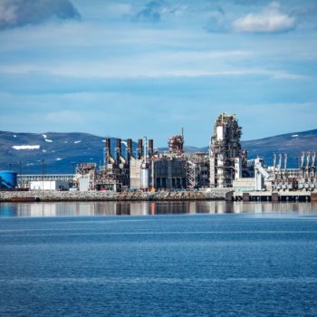 Hammerfest Island Muolkkut Northern Norway, gas processing plant. Industry on the water with snow-topped mountains in the background and a slightly cloudy sky.