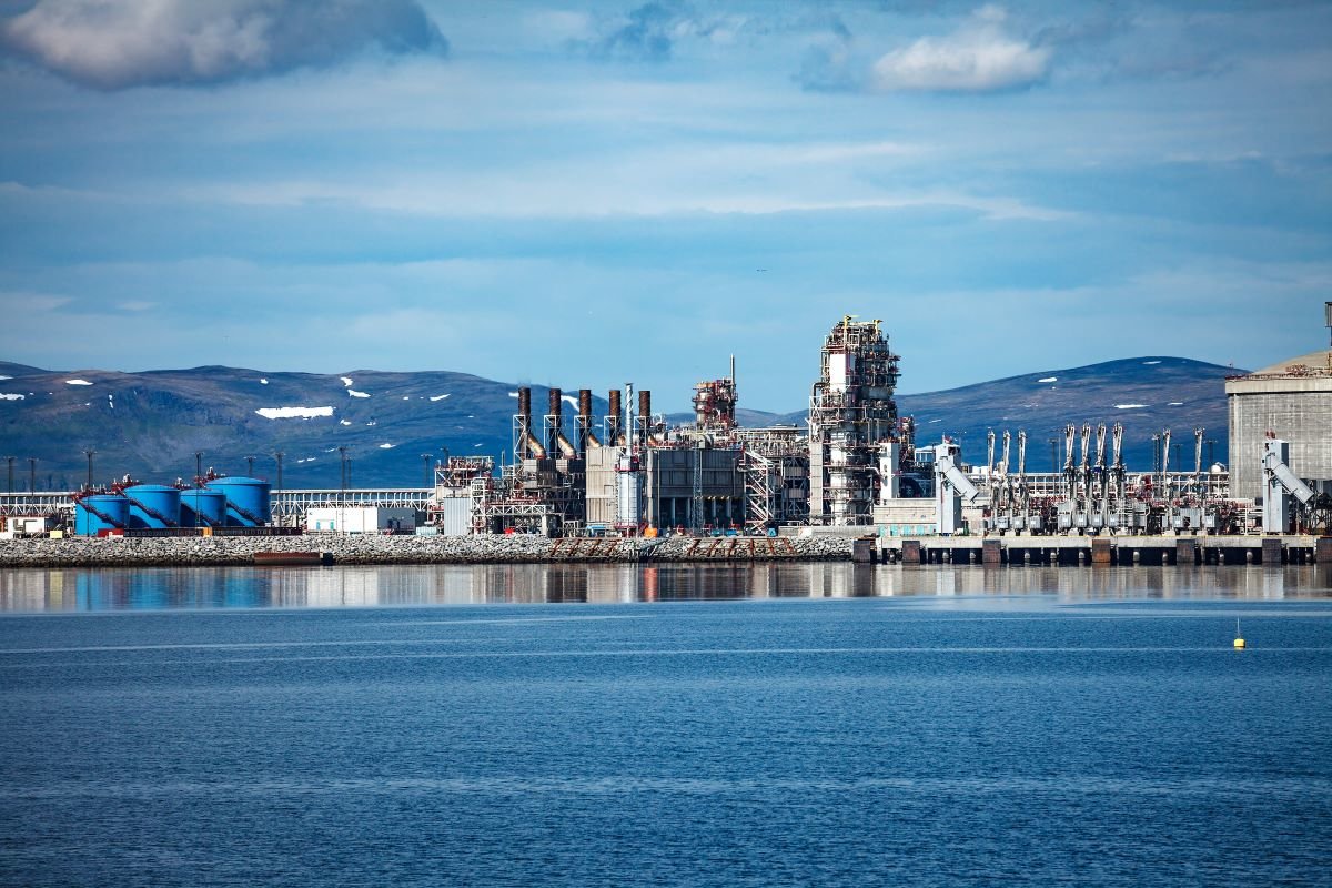 Hammerfest Island Muolkkut Northern Norway, gas processing plant. Industry on the water with snow-topped mountains in the background and a slightly cloudy sky.
