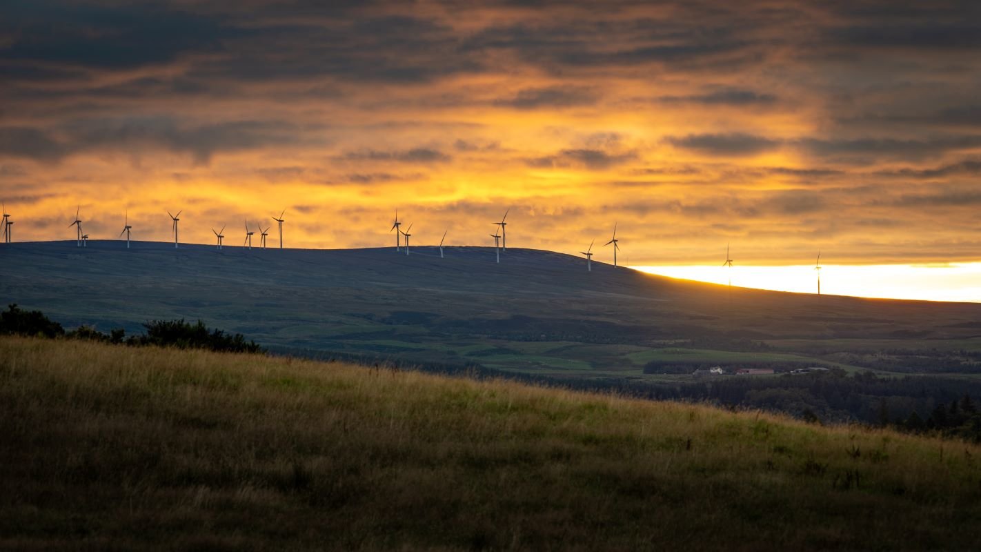 Image of sunrise and wind turbines on hills in Scotland.