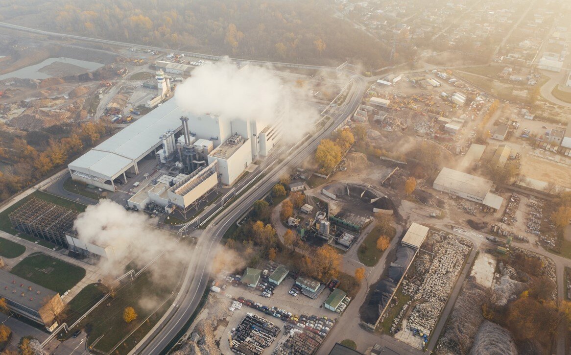 The image shows an industrial complex surrounded by clouds steaming from industrial emissions