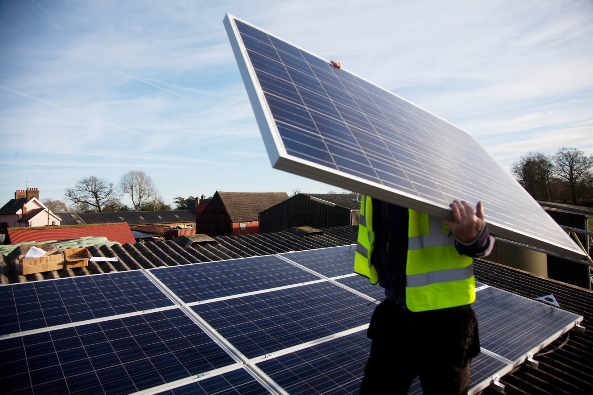 A builder holds a large solar panel in front of his face. Installing solar panels, a key part of energy security, on the roof of a home in Balcombe, UK.