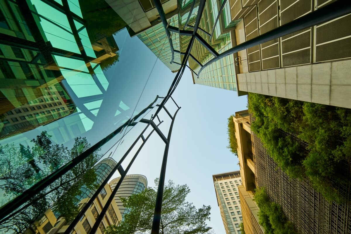 Looking up at modern design glass buildings with green and clear sky. Photo via Adobe.