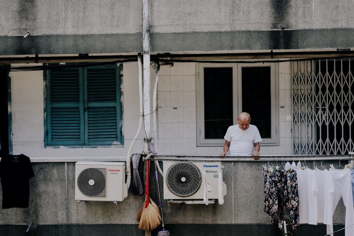 Man stands on a balcony of flat block with air conditioning units. Photo by Michu Đăng Quang on Unsplash