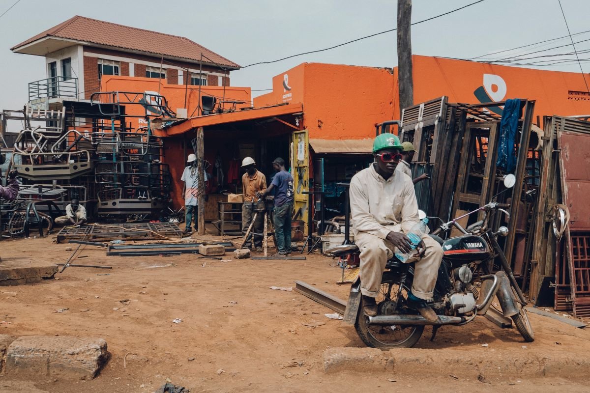 Mechanic sits on a motorbike by a stall selling car pats, Kampala, Uganda. Photo by Random Institute on Unsplash.