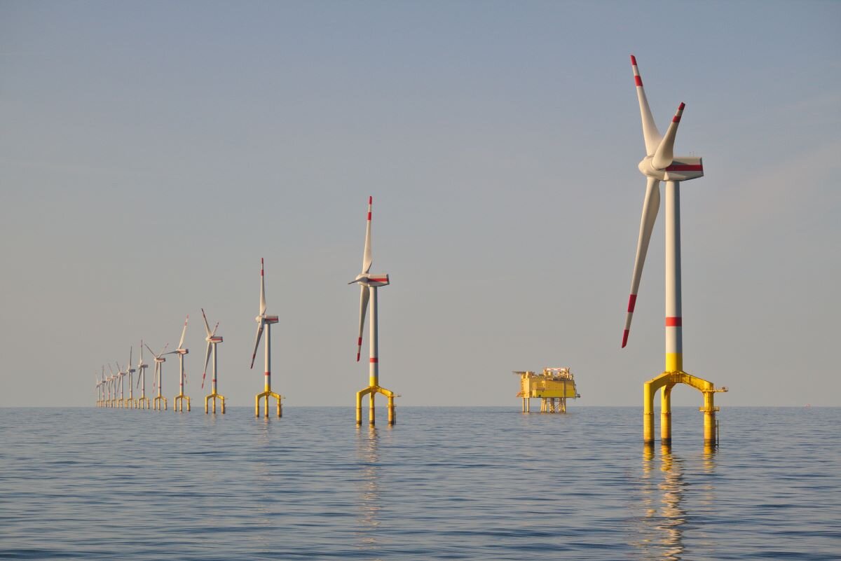 Offshore wind farm near the coast of France. Yellow and white windmills stretch out into the distance on a hasy day with blue sea and sky.