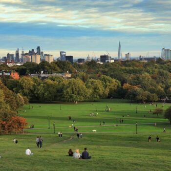People resting on Primrose Hill at sunset, London, UK, looking out over the City of London. Photo via Adobe.