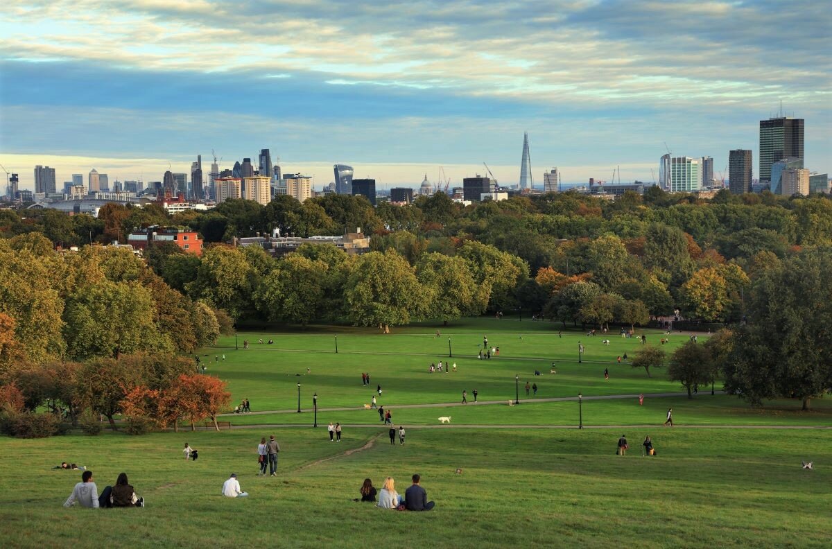People resting on Primrose Hill at sunset, London, UK, looking out over the City of London. Photo via Adobe.