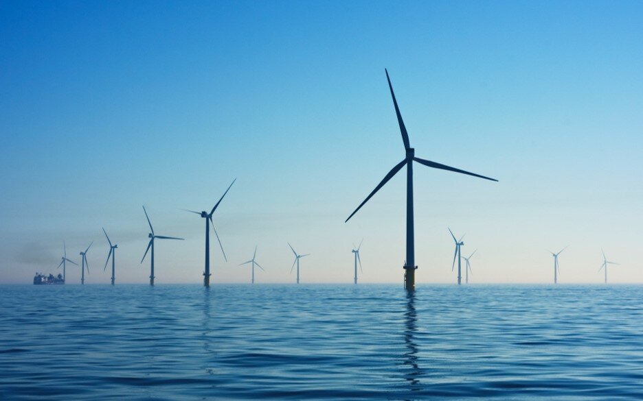 The image shows several windmills on a blue sea. It is Rampion's offshore wind farm, in the United Kingdom