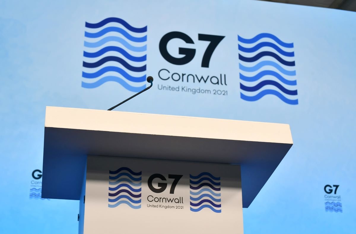 Photo of the pulpit at the press Conference Centre at the G7 Summit 2021. Taken from below. The G7 logo of blue waves can be seen on the pulpit and on the wall behind.