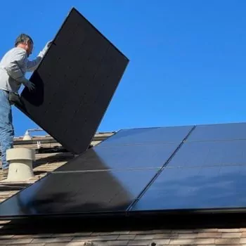 The image shows a man installing solar panels on the roof of a house