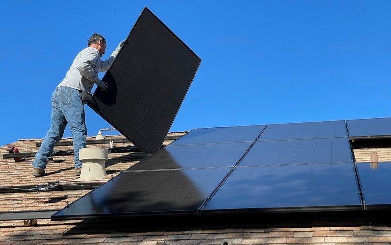 The image shows a man installing solar panels on the roof of a house