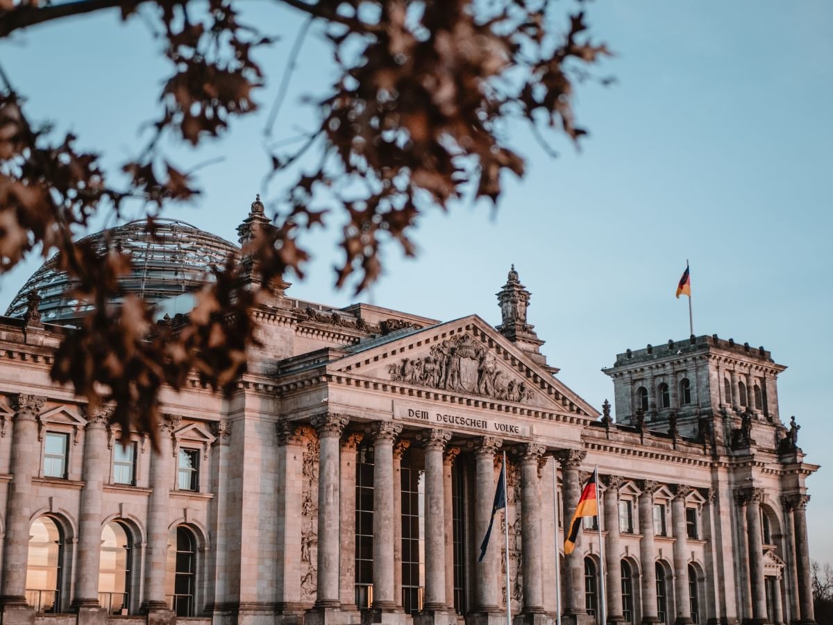 The Reichstag building, Berlin, the meeting place of the Bundestag or German federal government. The building is side on and against a blue sky. The light on the light on the building's grey stone front is dusky pink.