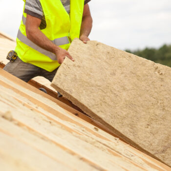 Two builders work together to install roof insulation. Energy efficiency measures like insulating UK homes is key to reducing gas demand. Photo via Adobe.