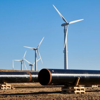 Two gas pipelines lie in front of a row of wind turbines at the construction site of the EU gas pipeline EUGAL near Wrangelsburg, Germany, in 2019. Photo via Adobe.