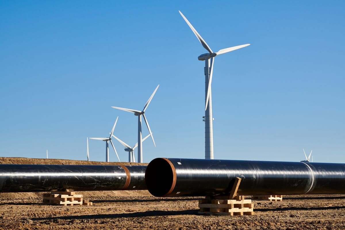 Two gas pipelines lie in front of a row of wind turbines at the construction site of the EU gas pipeline EUGAL near Wrangelsburg, Germany, in 2019. Photo via Adobe.