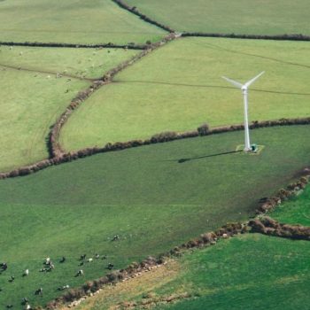 View from the sky of a wind turbine in green landscape of fields.