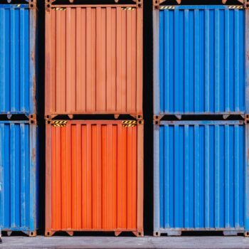 View of two workers cooperating in front of large red and blue corrugated iron containers from cargo freight ship for import export.
