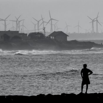 Wind turbines and two people standing by the ocean in Kanyakumari, Tamil Nadu, India. Black and white photo