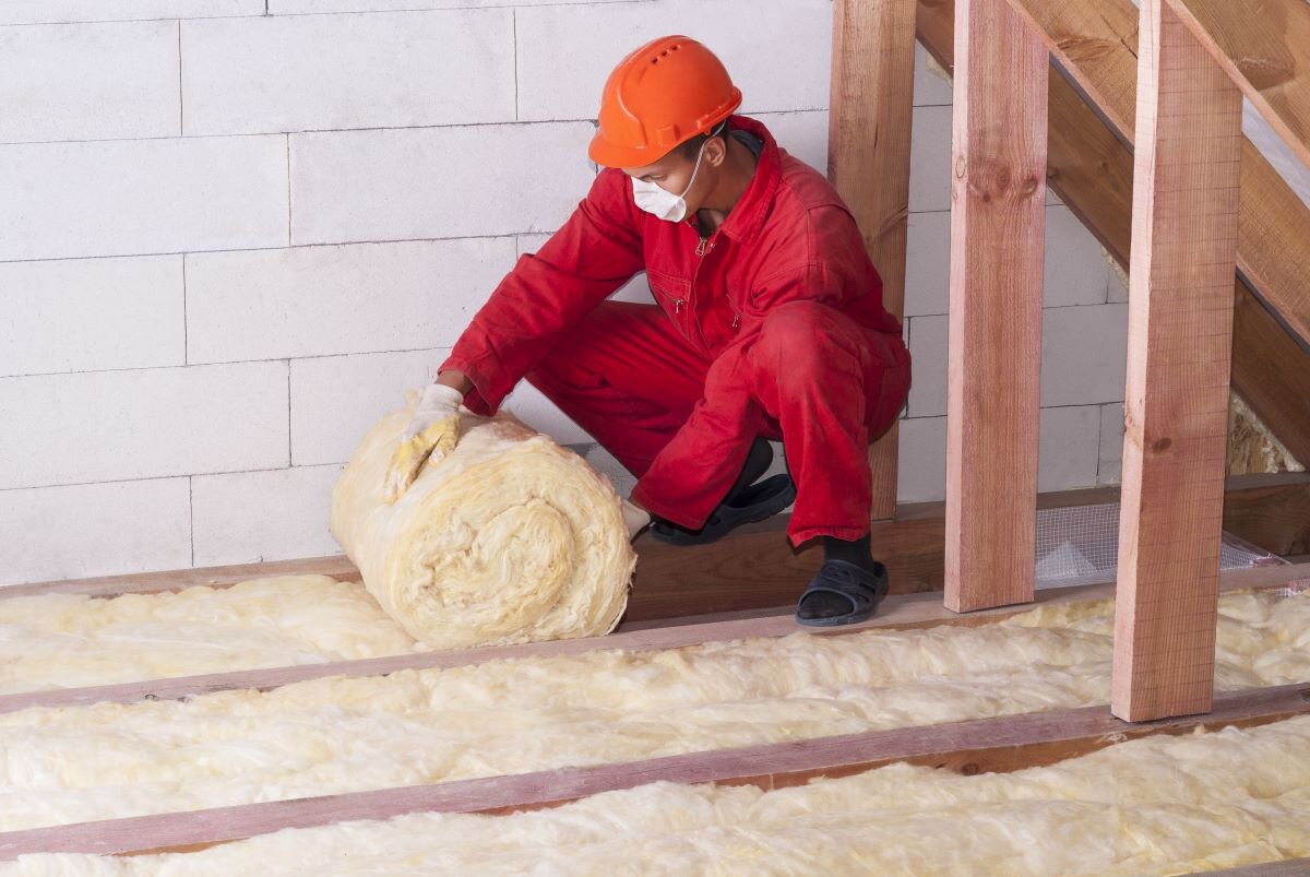 Worker dressed in red safety gear installs mineral wool packing for energy efficiency in a home. Energy saving insulation measures are a key part of the Energy Company Obligation.