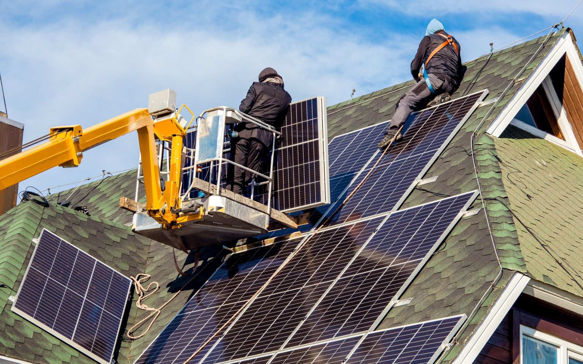 Workers installing solar panels on private home hexagonal roof felt on sunny day, blue sky. Photo via Adobe Stock.